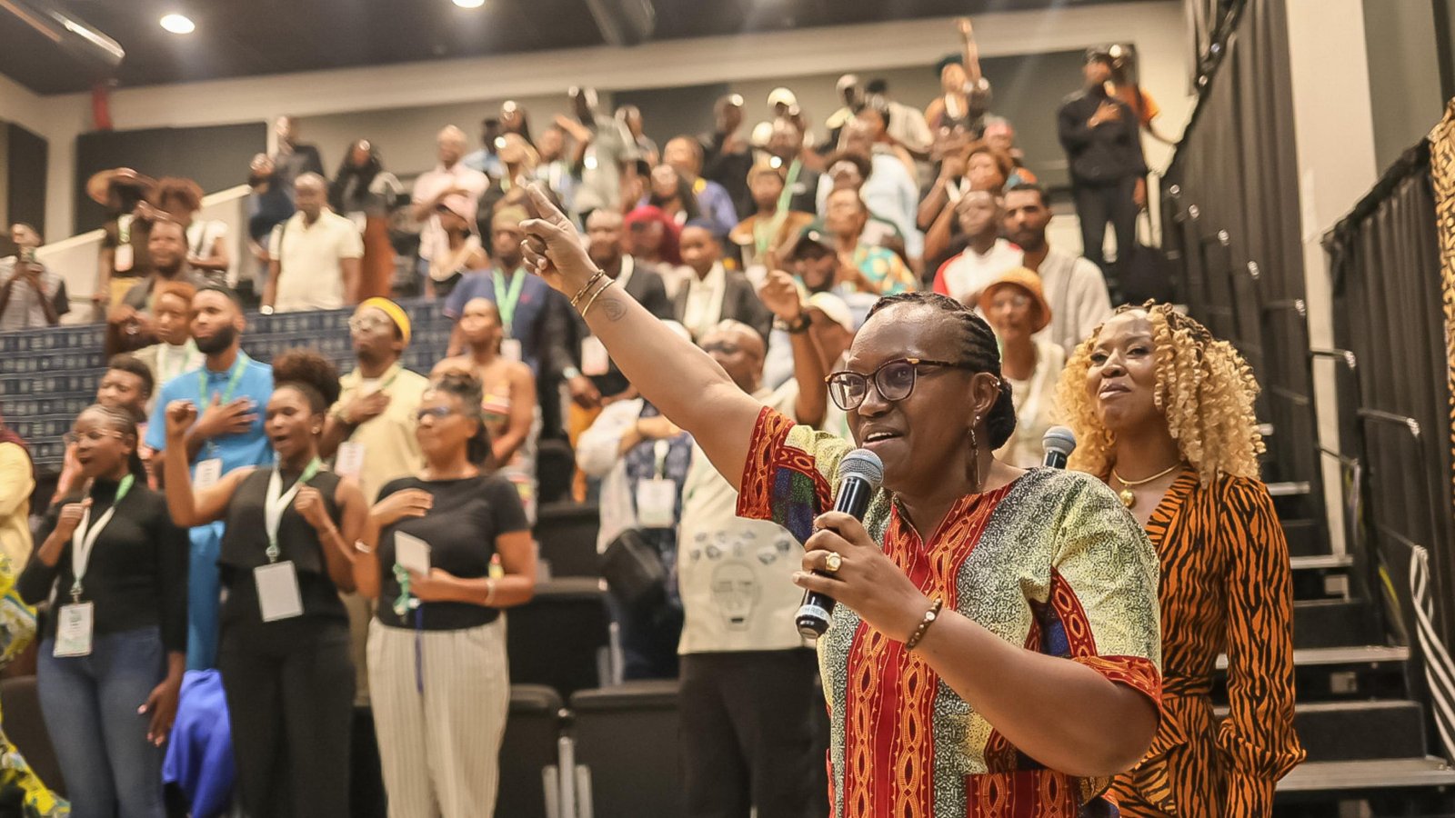 A delegate at the microphone with her arm raised as the room recites the Afrotellers Creed at the 2025 conference